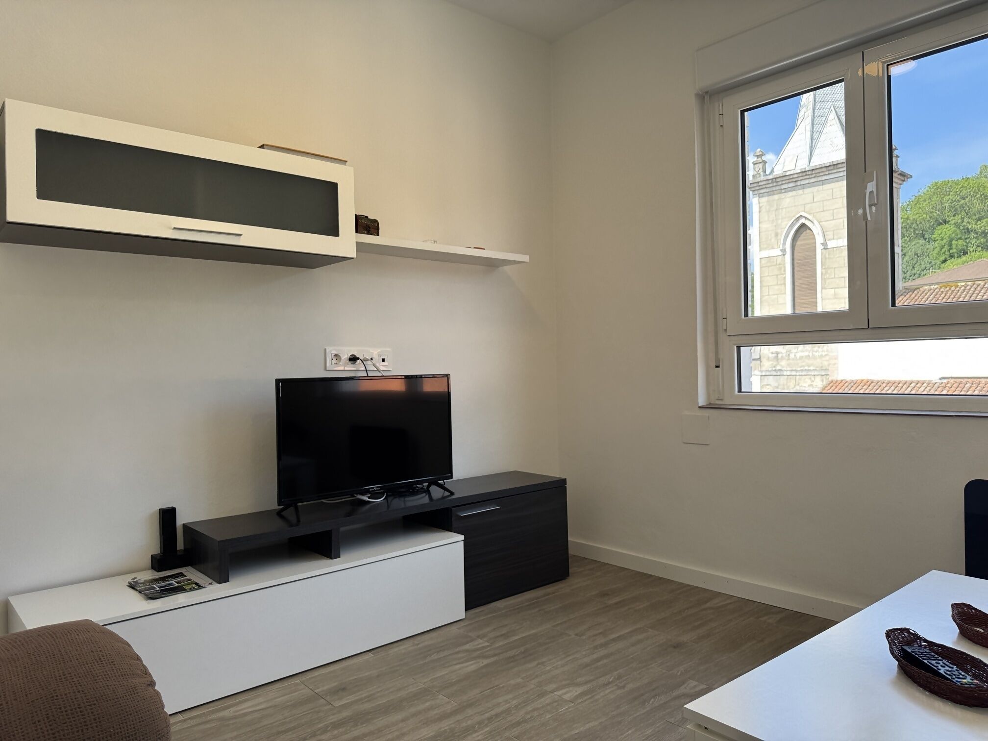Un salon moderne doté d’un téléviseur à écran plat, d’un petit meuble et d’une fenêtre donnant sur un immeuble.