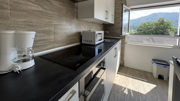 Une cuisine moderne avec un plan de travail noir, des armoires blanches, une machine à café, un four à micro-ondes et une vue sur les montagnes par une fenêtre.