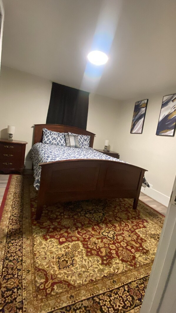Un dormitorio con cama, mesita de noche, lámpara, una obra de arte en la pared y alfombra estampada.