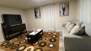 Una sala de estar con sofá, una mesa de centro, televisor y alfombra estampada.