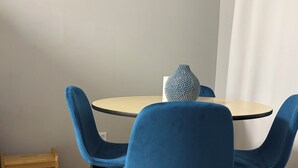 Spisestue med et rundt bord, fire blå stole, et lille træsidebord og en dekorativ vase.