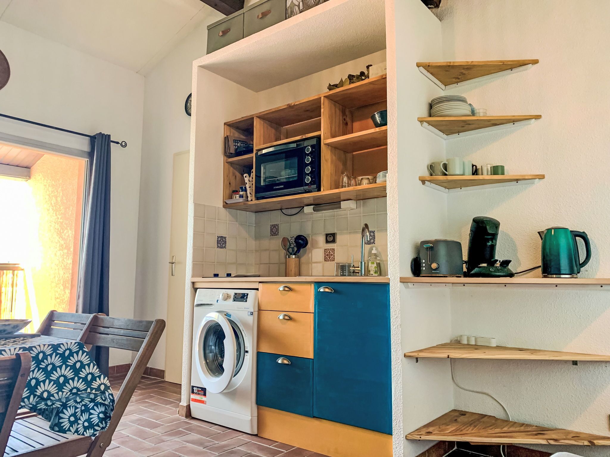 Een kleine keuken met een wasmachine, magnetron en houten planken.
