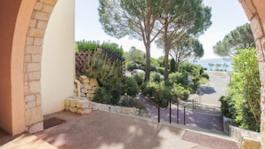 A balcony with a stone wall, a view of a tree, and a road leading to a body of water. - La Gaillarde by Interhome (Les Issambres)