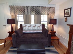 A cozy living room with a brown sofa, two side tables with lamps, a patterned throw pillow, and a window with curtains.