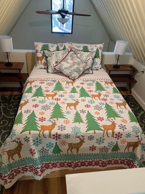A bedroom with a bed covered in a festive quilt, two bedside tables with lamps, a window with a view of trees, and a ceiling fan. - Norwegian-Inspired Pocono Log Cabin, Cozy Woodland Escape & Fire Pit (Mountainhome)