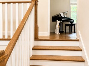 A staircase with wooden steps and white railings leading to a room with a grand piano.