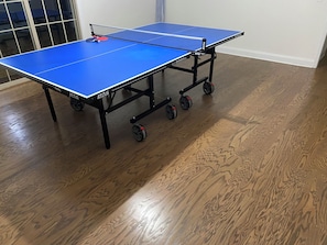 Une table de ping-pong bleue, munie de roulettes, posée sur un plancher en bois.