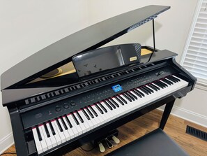 Un piano à queue doté d’un écran numérique, placé dans une pièce au plancher en bois et comportant une fenêtre avec des stores.