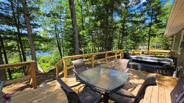 A wooden deck with a glass table and chairs, a hot tub, and a view of a forest and lake. - Foreman Lakefront Cabin Hot Tub Wi-Fi Dog Friendly (Idlewild)