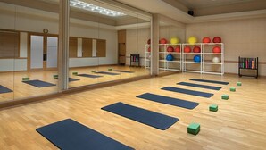 Una habitación amplia con suelo de madera, espejos grandes y colchonetas de ejercicio dispuestas para actividades físicas.