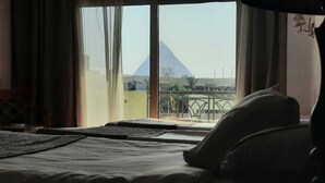 Una camera d'albergo con un letto, una finestra che si affaccia su una piramide e un balcone con ringhiera.