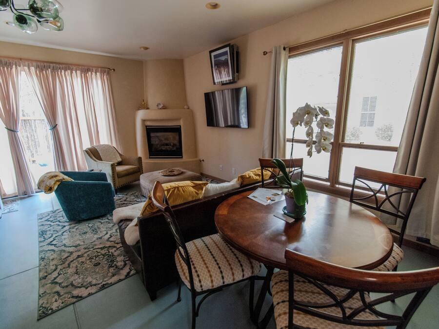 A living room with a sofa, a dining table with chairs, a fireplace, and a large window with curtains.