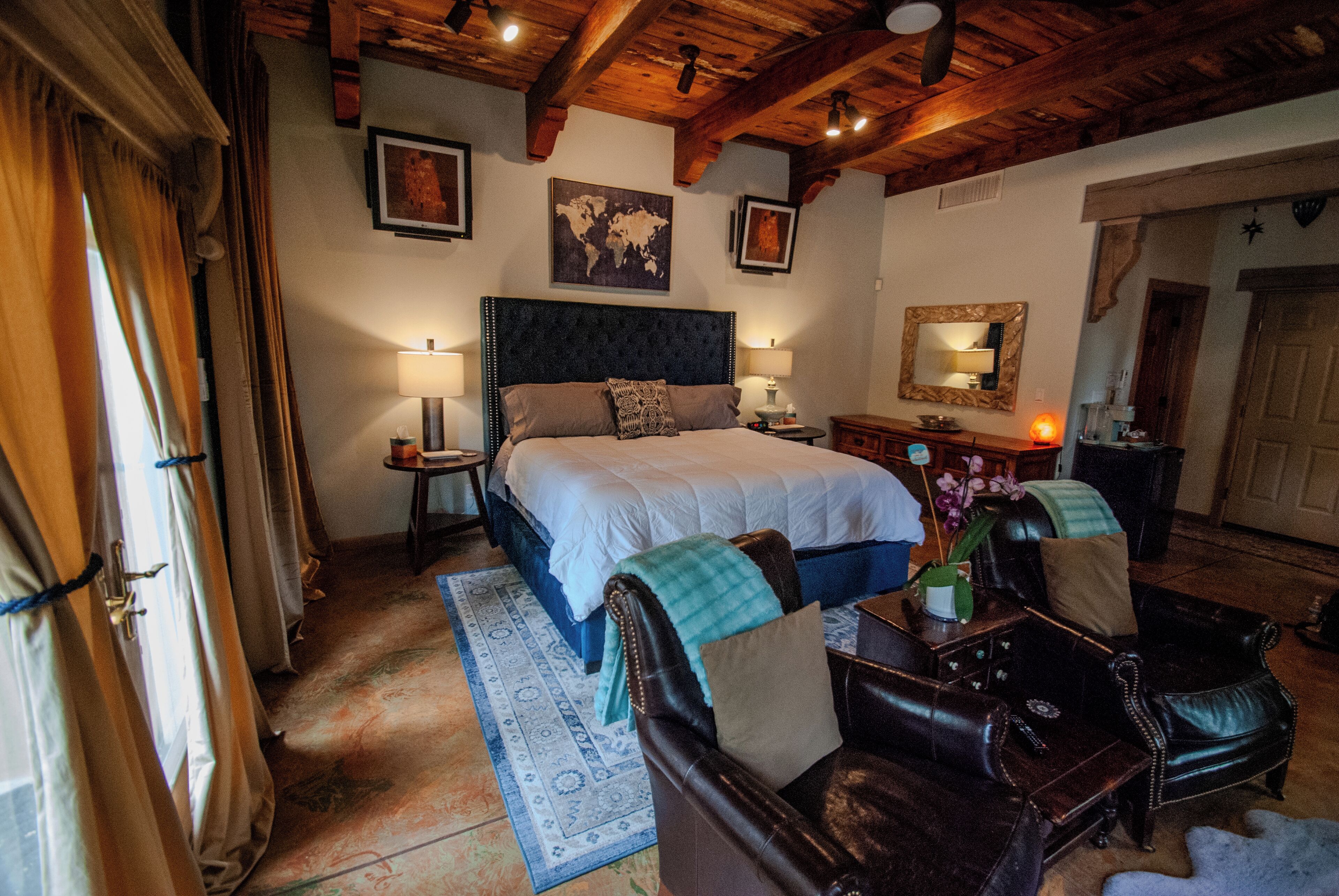 A bedroom with a large bed, two bedside tables, a dresser, a mirror, and a wooden ceiling.