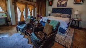 A bedroom with a large bed, leather chairs, a rug, and a wooden floor.