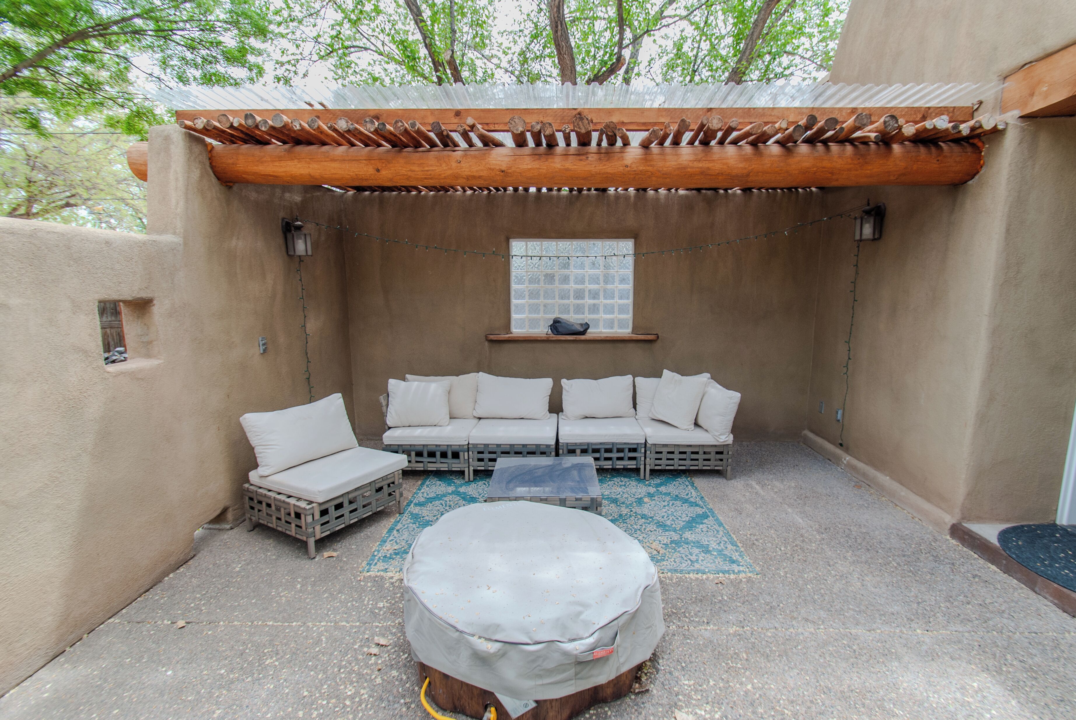 A covered outdoor seating area with a wooden pergola, a sofa set, and a round table.