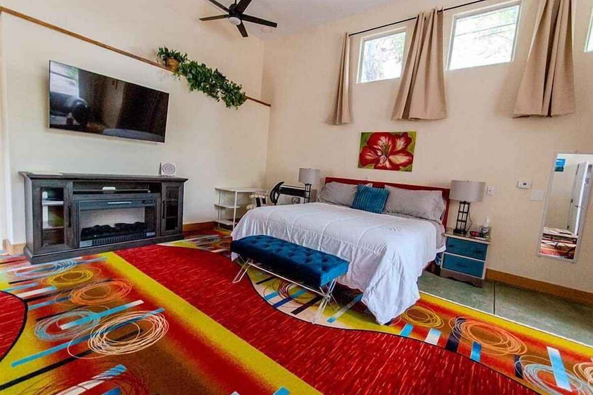 A bedroom with a bed, a TV, a desk, and a colorful carpet.
