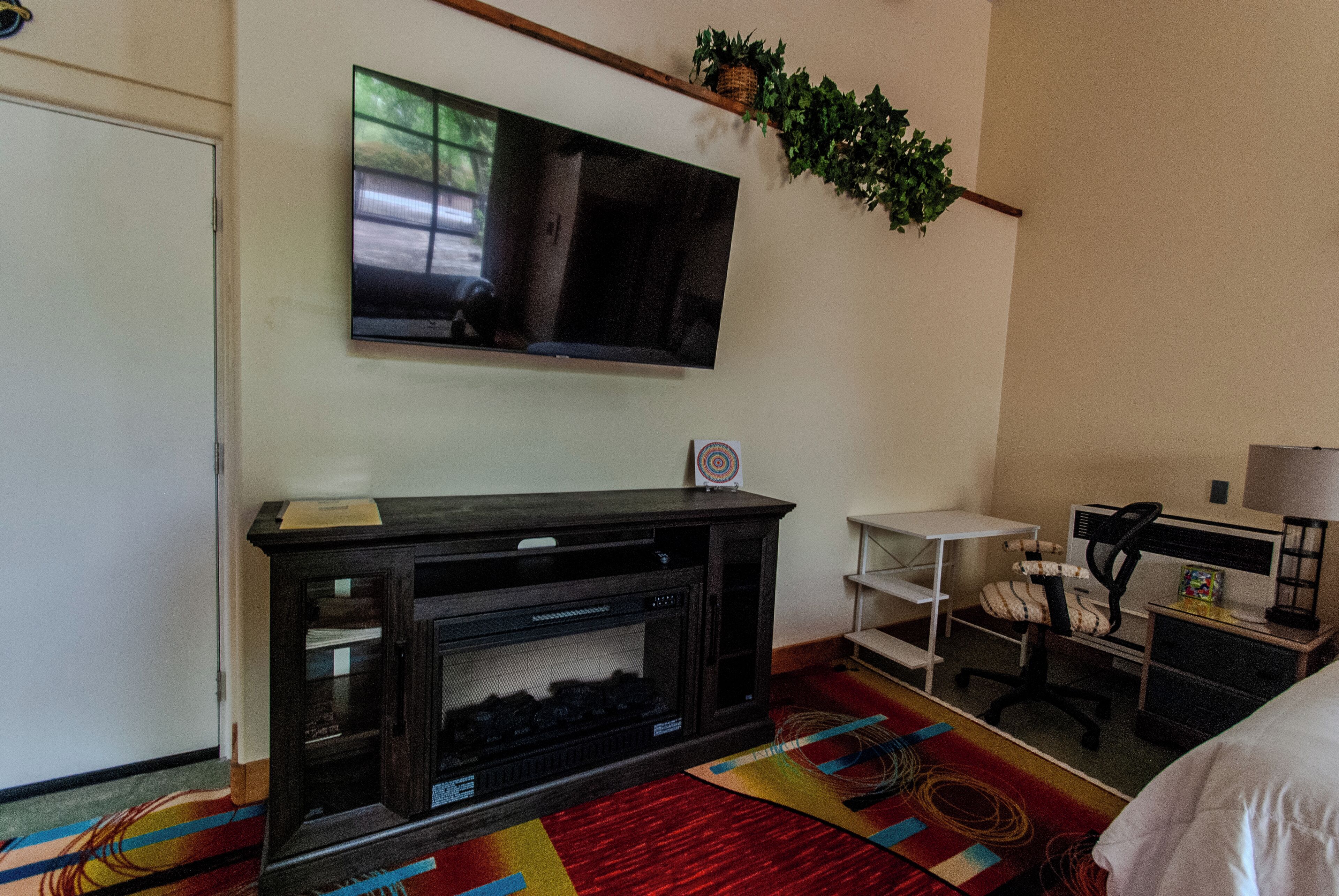 Habitación de hotel con televisión de pantalla plana en la pared, chimenea, escritorio con silla y cama.