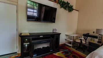 Habitación de hotel con televisión de pantalla plana en la pared, chimenea, escritorio con silla y cama.