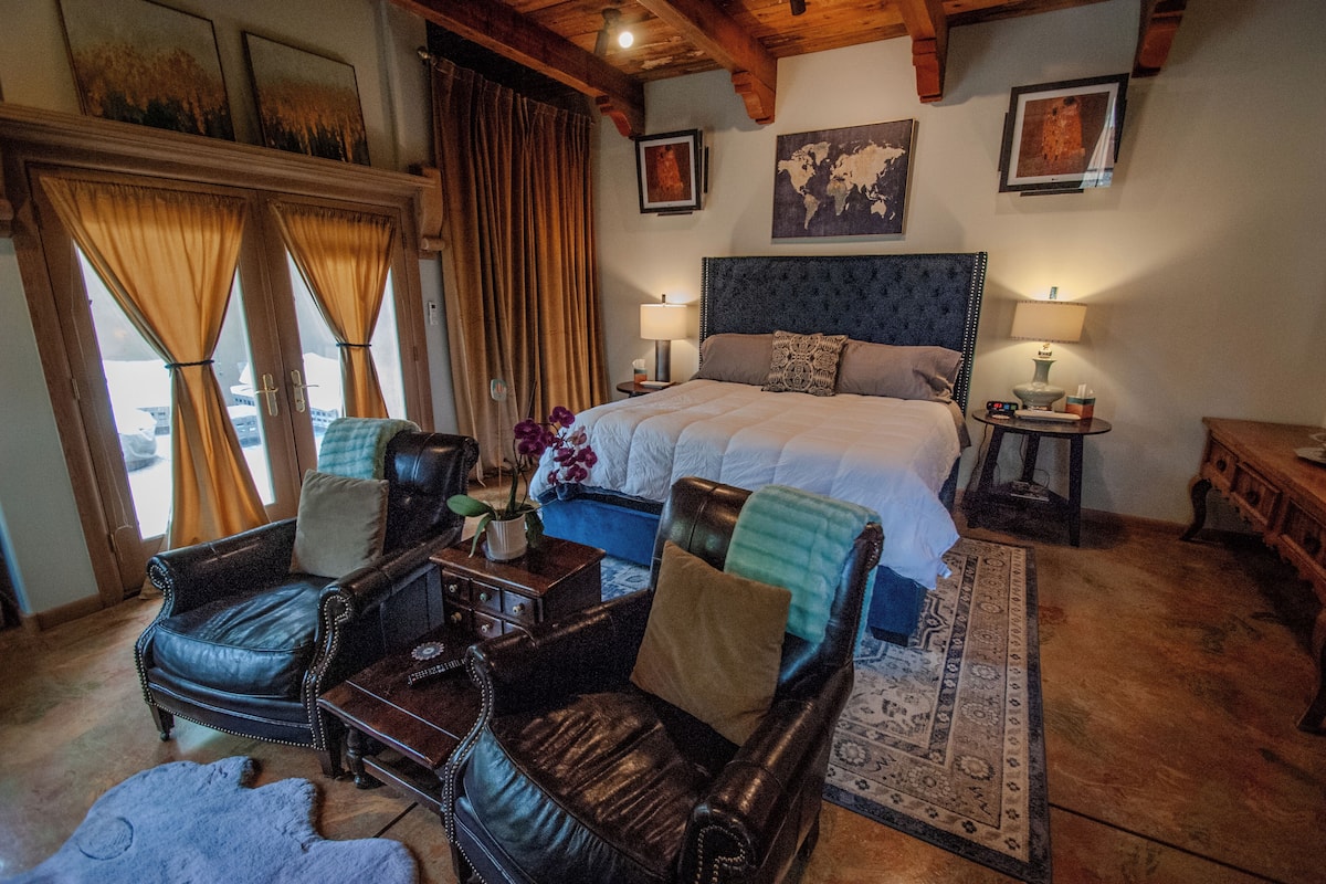 A bedroom with a large bed, two leather chairs, a small table, and a rug.