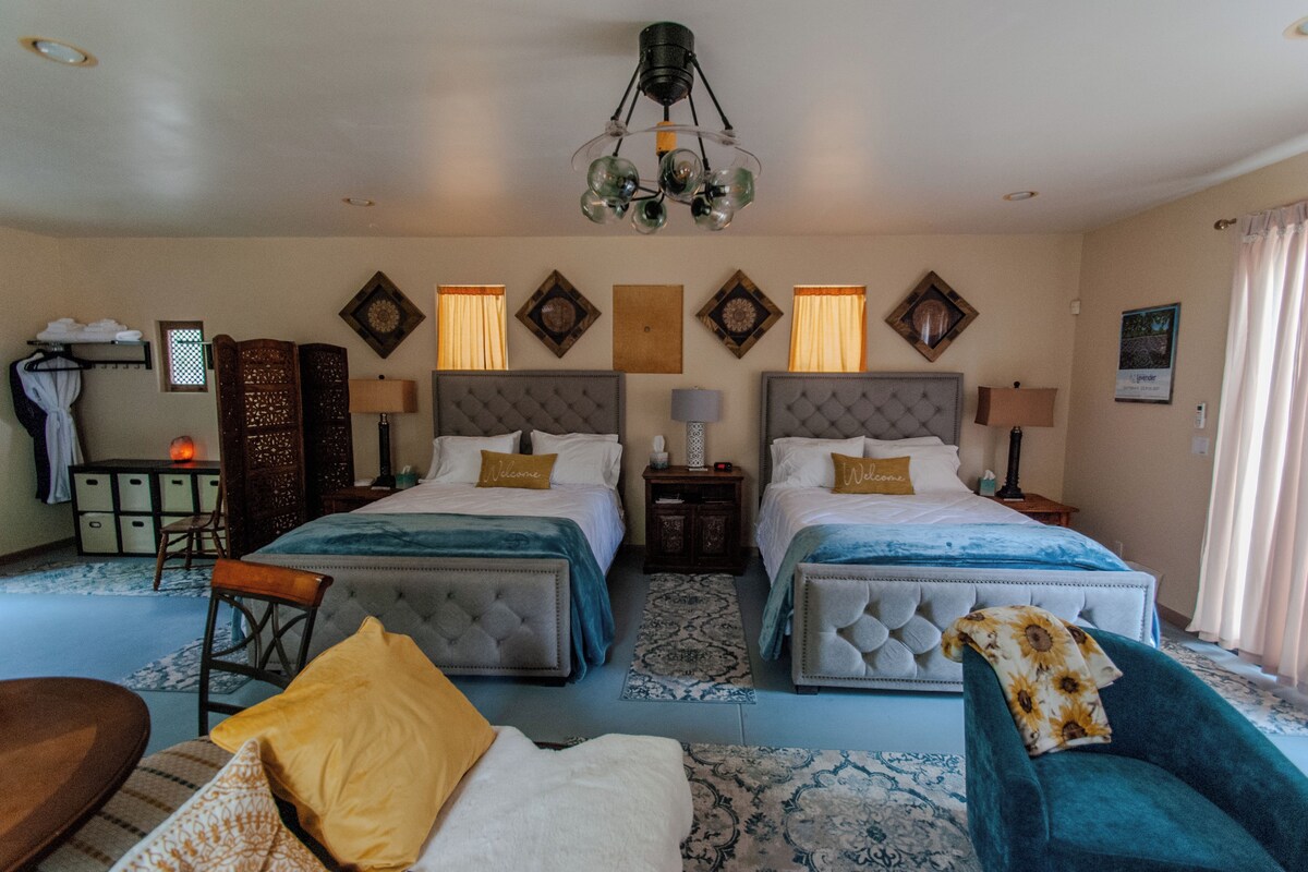 A hotel room with two beds, a desk, a chair, and a decorative chandelier.