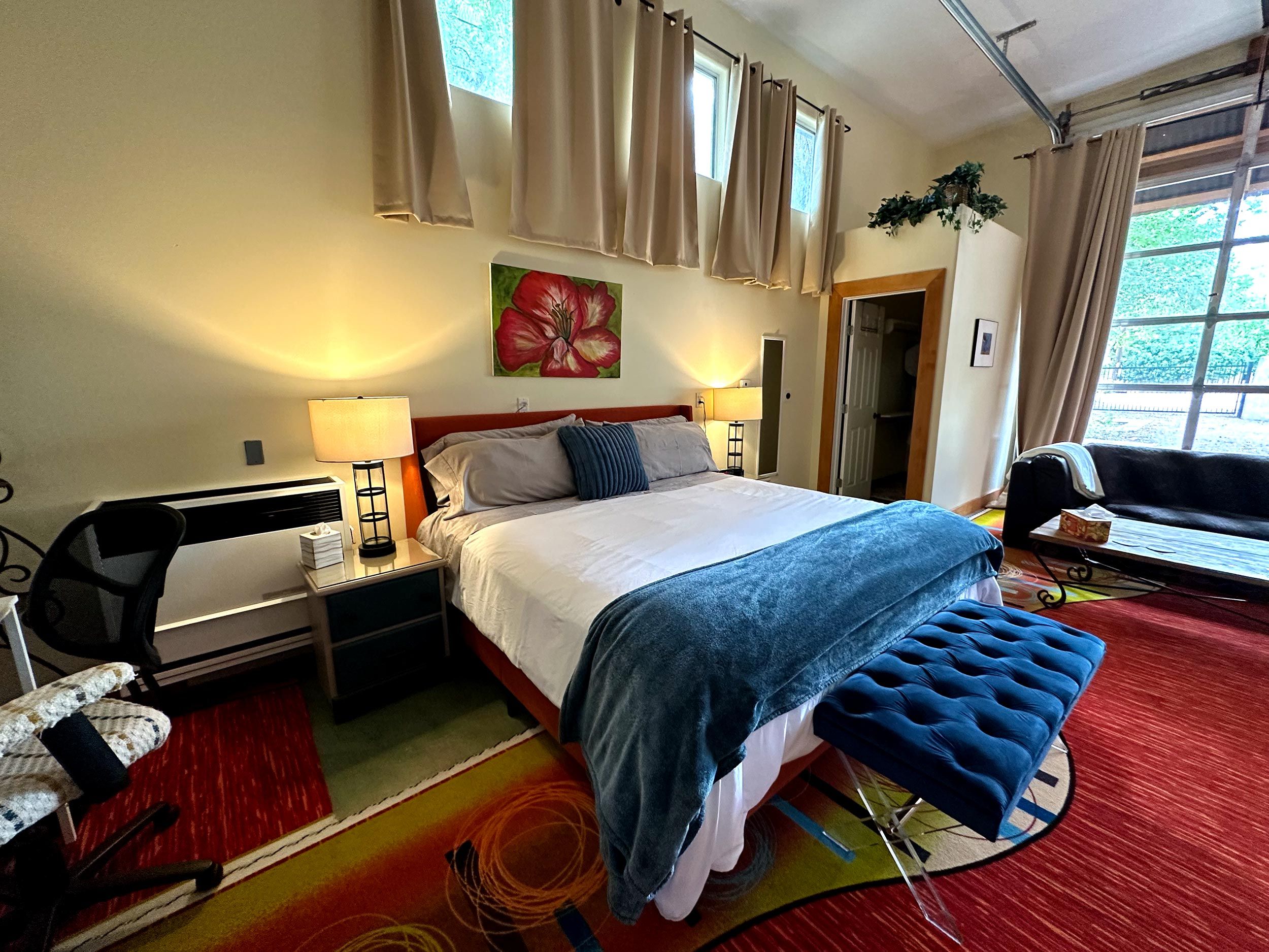 Quarto de hotel com cama, abajures, uma poltrona, sofá e janela com cortinas.