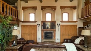 A spacious living room with a fireplace, wooden beams, and large windows.