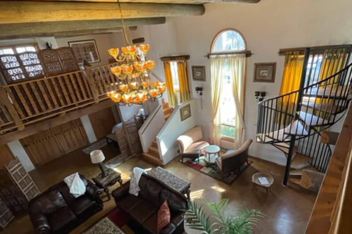 A spacious living area with a staircase, leather sofas, a chandelier, and a large window with curtains.