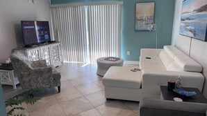 A living room with a TV, white sofa, patterned armchair, and a ceiling fan. - Great 2 BR Condo, 7 minutes to Siesta Key (Sarasota)