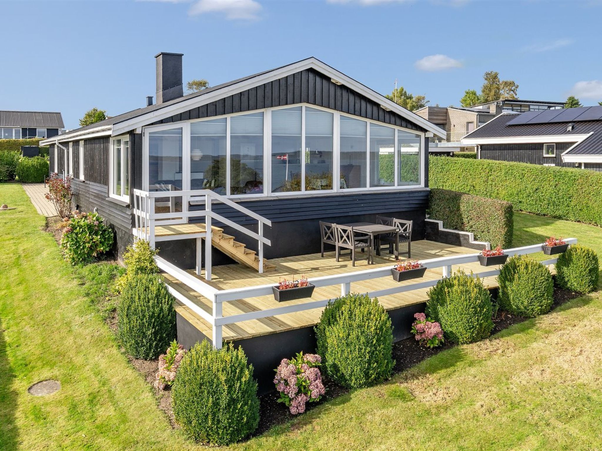 A modern house with a large deck, a covered patio, and a well-maintained garden.