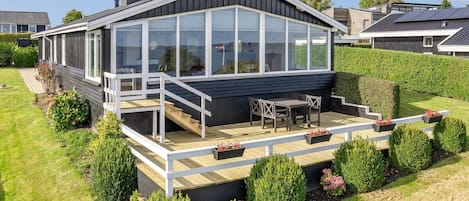 A modern house with a large deck, a covered patio, and a well-maintained garden.