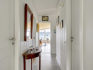 Een gang met witte muren, een houten console en glaswerk, en ingekaderde foto’s.
