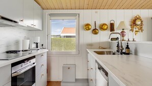 Eine moderne Küche mit weißen Schränken, einer Holzbalkendecke und Blick auf ein Haus durch ein Fenster.