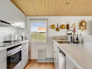Een moderne keuken met witte kastjes, een houten plafond en uitzicht op een huis door een raam.