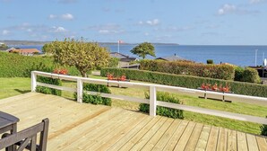 Eine Holzterrasse mit weißer Geländer, die auf ein Gewässer mit einer entfernten Küste blickt.
