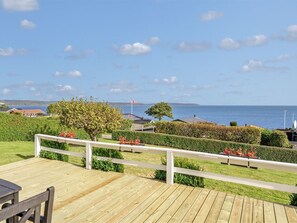 Een houten terras met een witte balustrade, uitkijkend op een waterpartij met een verre oever.