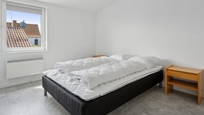 Ein Schlafzimmer mit einem Bett, einem Fenster und einem kleinen Nachttisch.