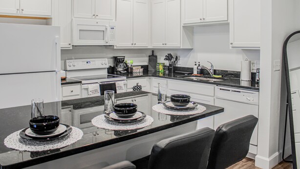 A modern kitchen with white cabinets, a black countertop, and a dining area with two chairs.