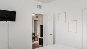 A bedroom with a bed, a door leading to another room, and a wall-mounted TV.