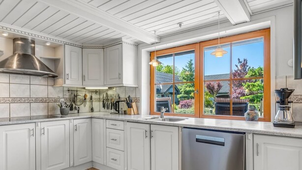 A modern kitchen with white cabinets, a stainless steel dishwasher, and a large window with a view of the outdoors.