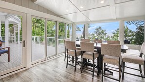 Un comedor amplio con una mesa grande y sillas, ventanas panorámicas que ofrecen vistas al exterior y un patio cubierto con una escalera que conduce a un nivel superior.
