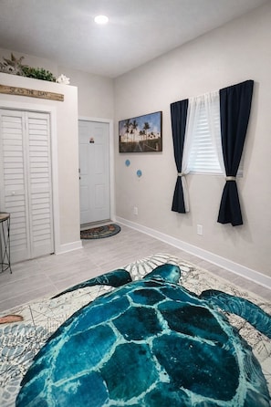 Quarto com cama, porta, quadro na parede e janela com cortinas.