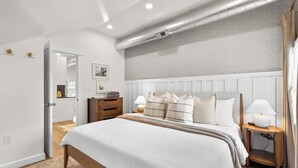 A modern bedroom with a large bed, bedside tables, a mirror, and a ceiling vent.