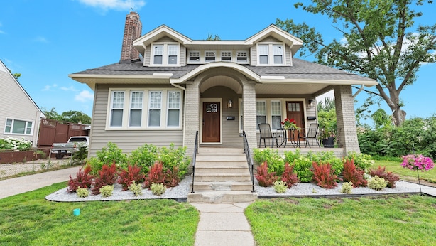 A two-story house with a front porch, a chimney, and a driveway leading to a parked truck.