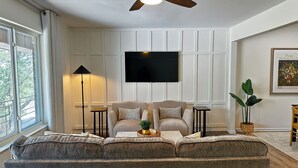 Ein Wohnzimmer mit einer Couch, zwei Sesseln, einer Stehlampe, einem Deckenventilator, einem Flachbildfernseher und einem gerahmten Bild an der Wand.