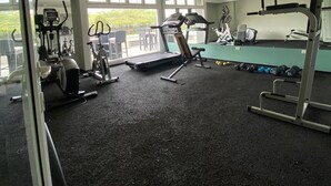 A gym with various exercise equipment, large windows, and a view of greenery outside.