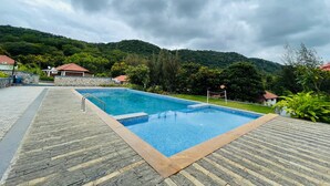 Una piscina rectangular amb una terrassa de pedra al voltant, amb un fons de turons verds i un cel amb núvols.