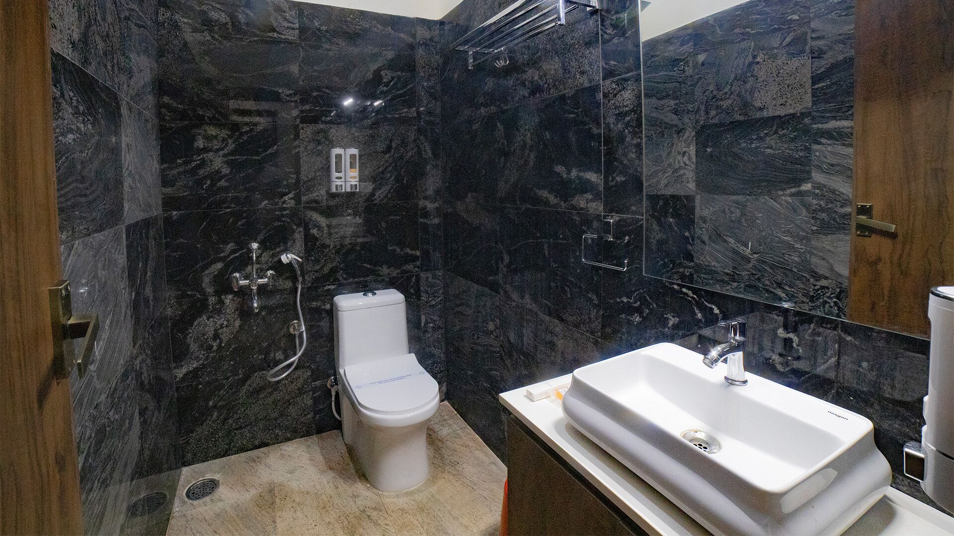 Un baño moderno con paredes de mármol oscuro, un inodoro blanco y un lavamanos grande de color blanco.