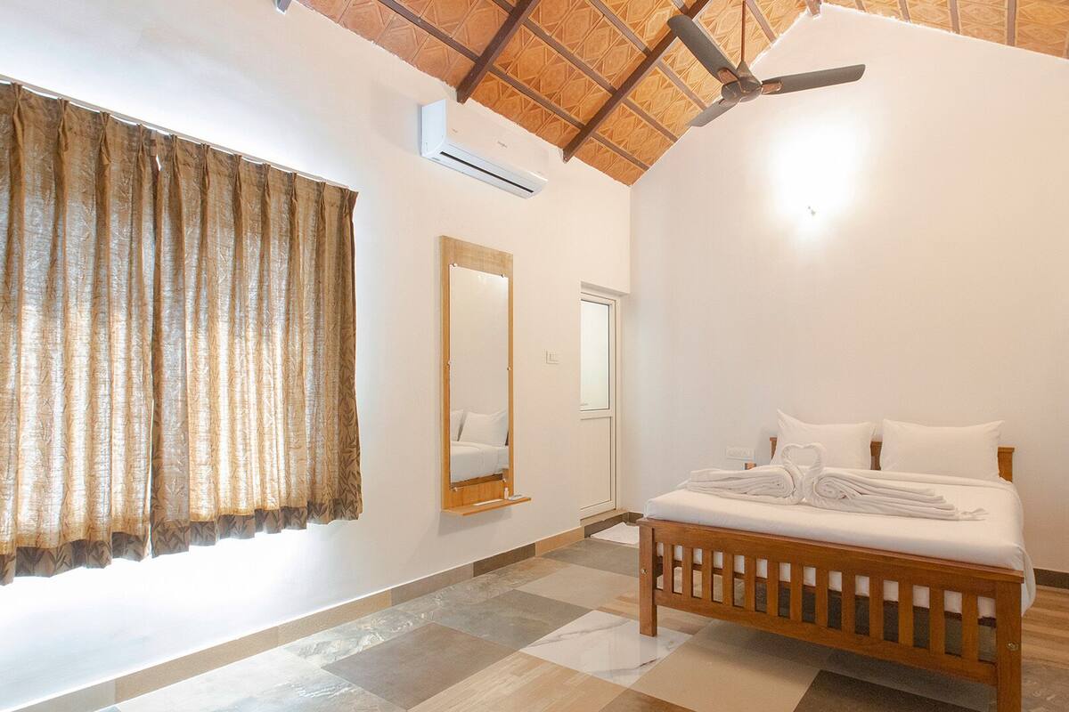 Une chambre à coucher avec un lit, un miroir, un ventilateur de plafond et une fenêtre avec des rideaux.