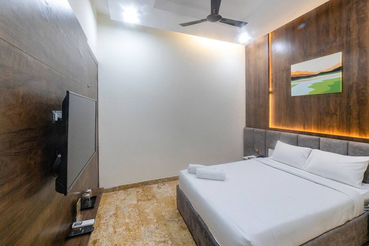 Une chambre d’hôtel avec un lit, un téléviseur à écran plat fixé au mur, un ventilateur de plafond et un tableau au-dessus du lit.
