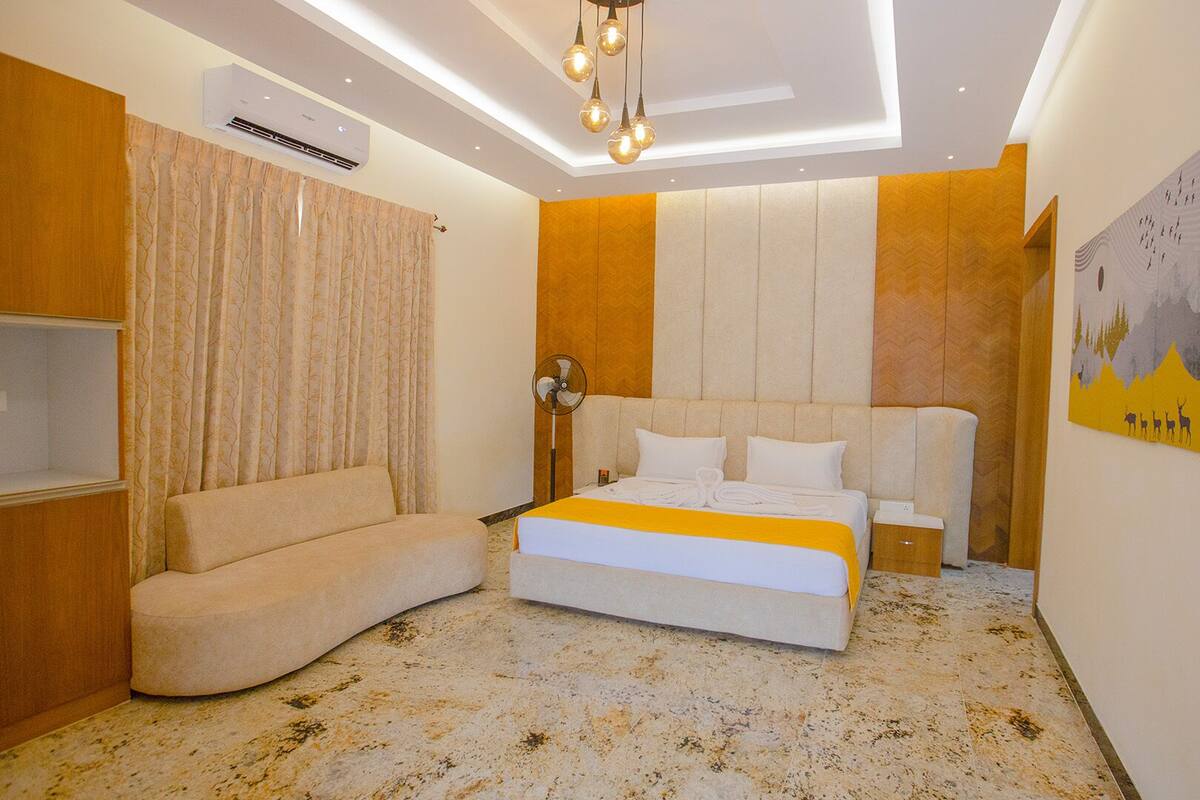 Une chambre moderne équipée d’un lit, d’un canapé, d’un ventilateur de plafond et d’un climatiseur fixé au mur.